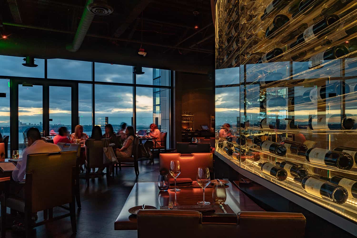 Bellevue steakhouse with display of vintage fine wines and view of Lake Washington with patrons enjoying wine and browsing curated menu