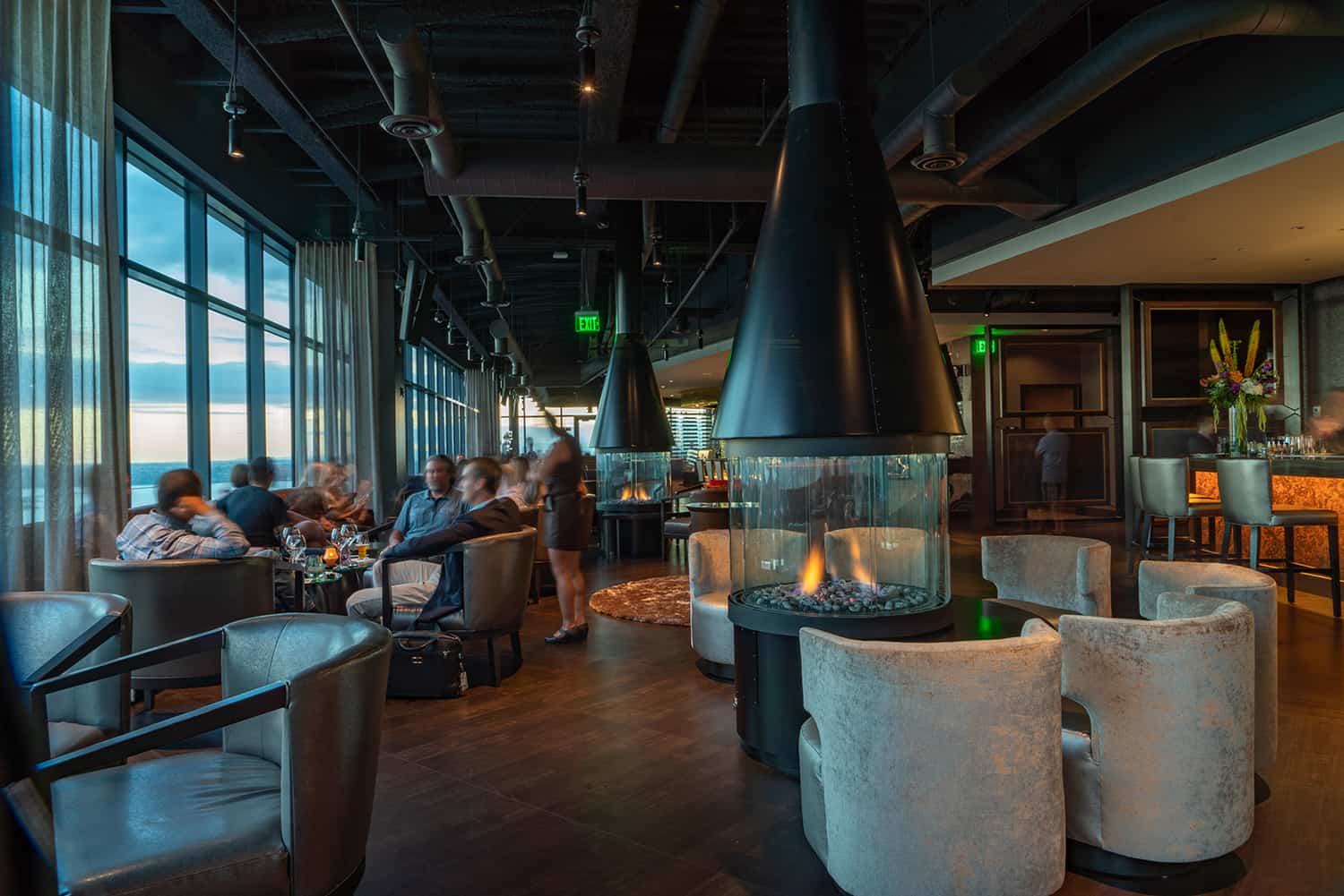 Bellevue steakhouse lounge with comfortable chairs around fireplaces and patrons enjoying a view of Lake Washington