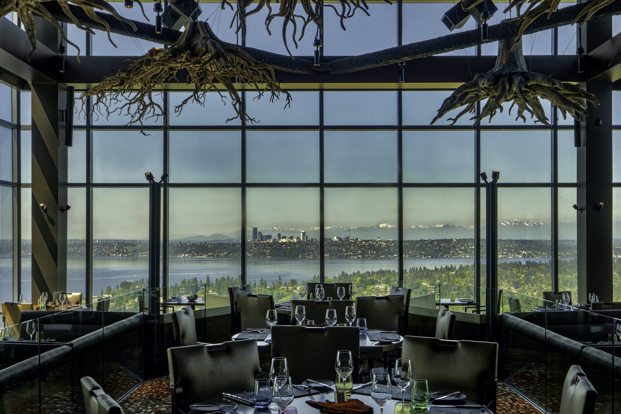 Bellevue steakhouse dining room with view of Lake Washington and tables filled with wine glasses below tree trunk decor