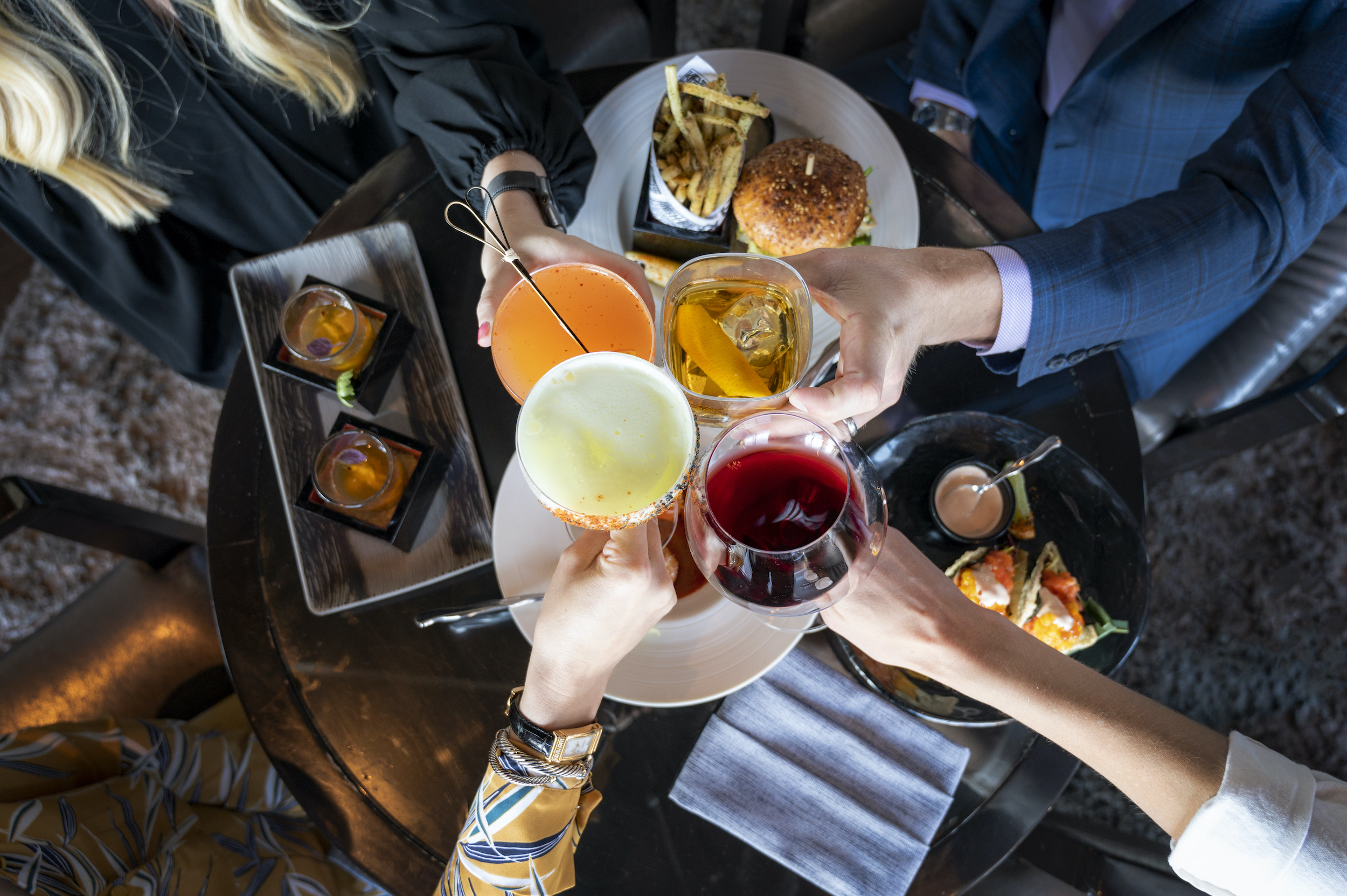 Guests enjoying Happy Hour with a spread of different bites and a cocktail cheers. 