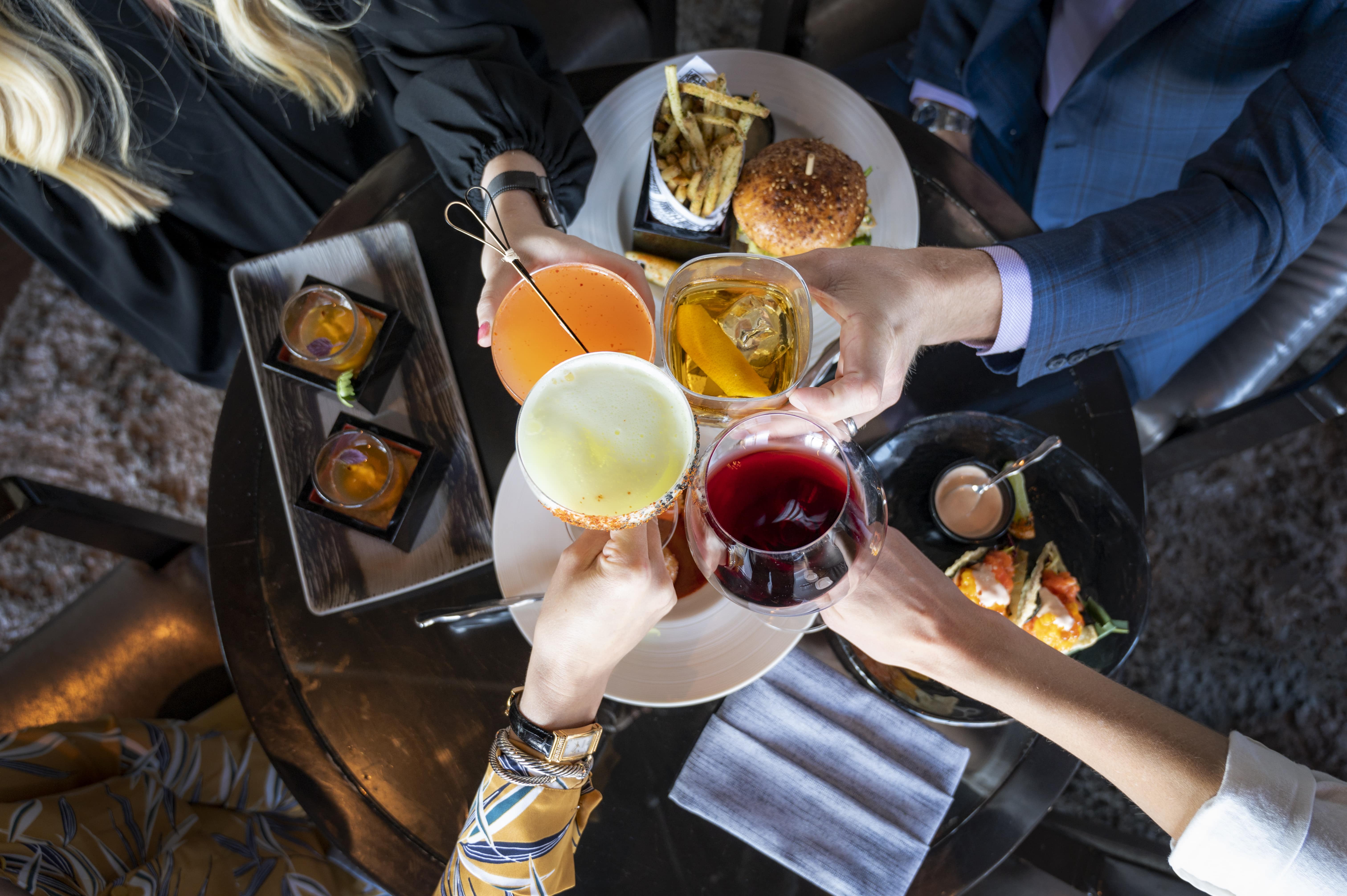 Happy hour at Bellevue fine dining restaurant with patrons making toast with craft cocktails, wagyu burger, and appetizers