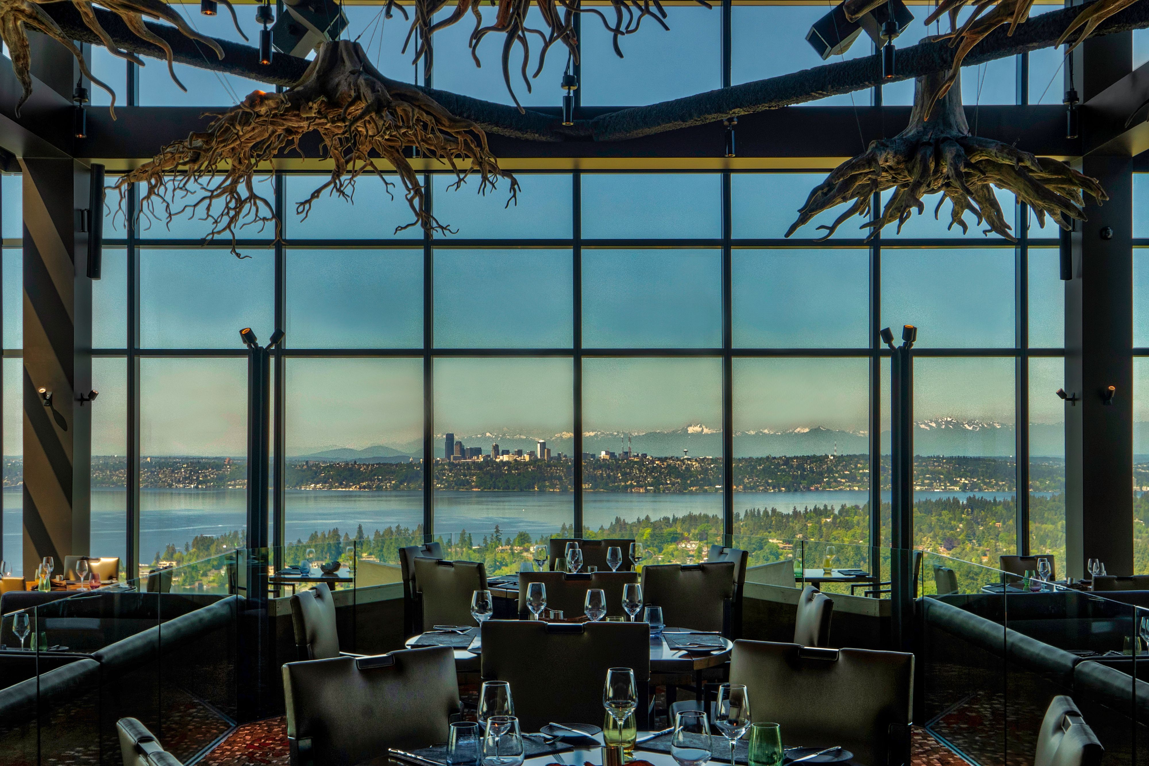 Bellevue restaurant dining room overlooking forest, Lake Washington, and Seattle skyline with wine glasses on tables and tree trunk decor above